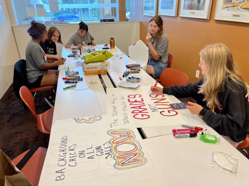 Five young women sitting around a table writing on poster board. 