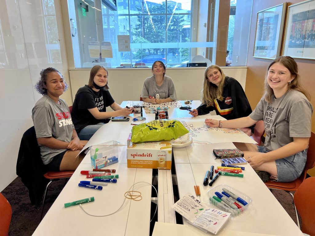 Five young women sitting around a table smiling. 