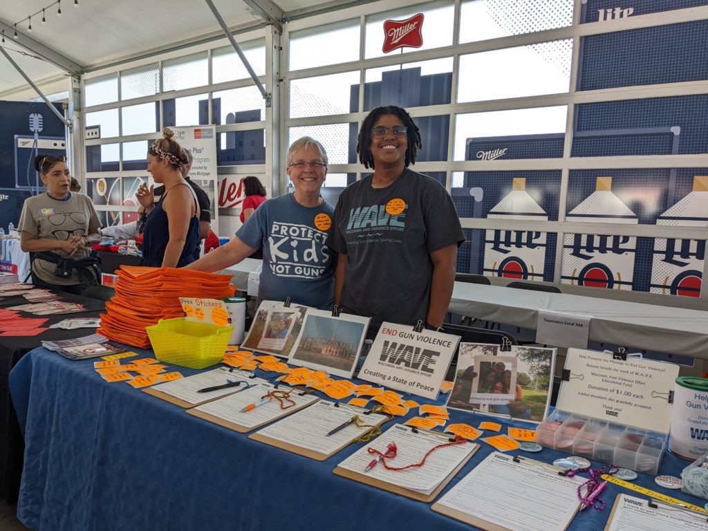 Two WAVE employees smile at the camera from behind a table covered with literature 